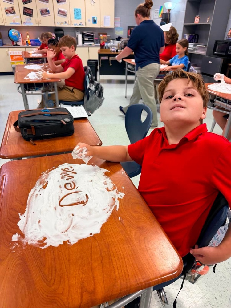 Mrs. Allen’s student writing spelling words in shaving cream on their desk in the classroom. 