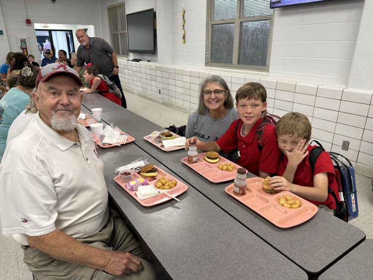 grandparents and students eating breakfast in the cafeteria in the school. 