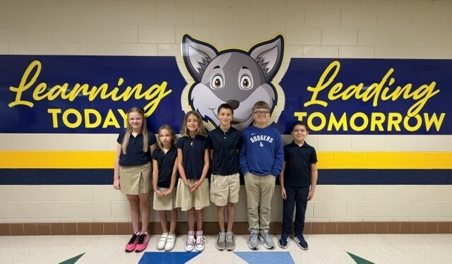 A group of children stands in a corridor, with a school mascot above them on the wall.