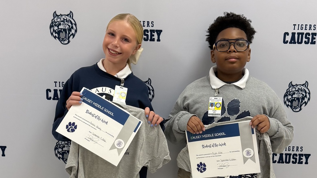 Two kids in blue and gray sweaters, smiling and holding certificates with their names on them.