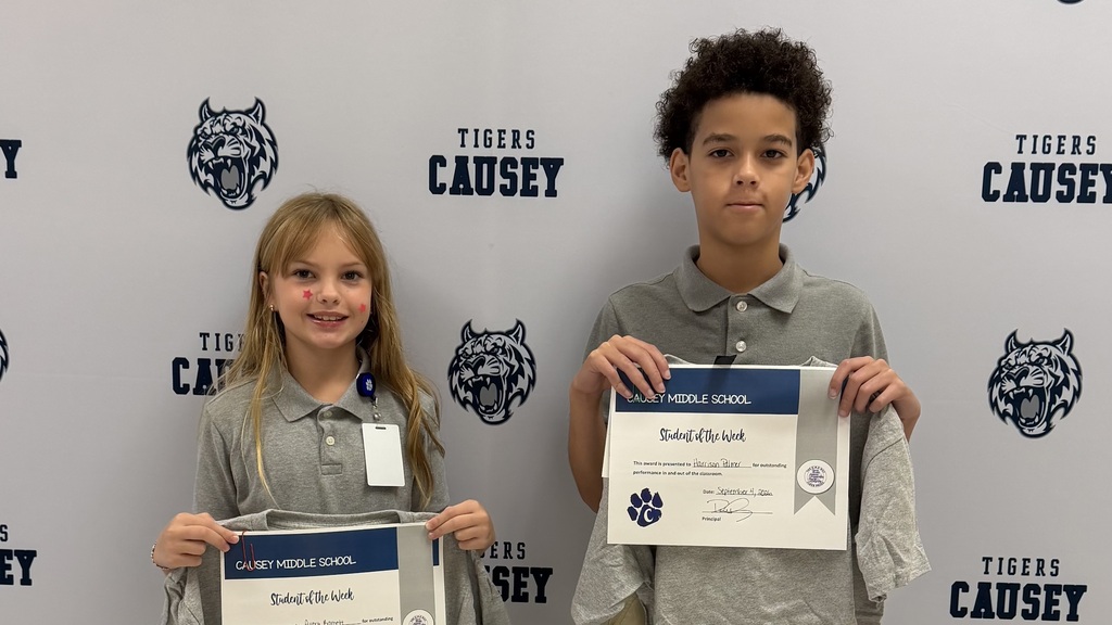 Two children in gray shirts hold certificates in front of a wall with logos and text.