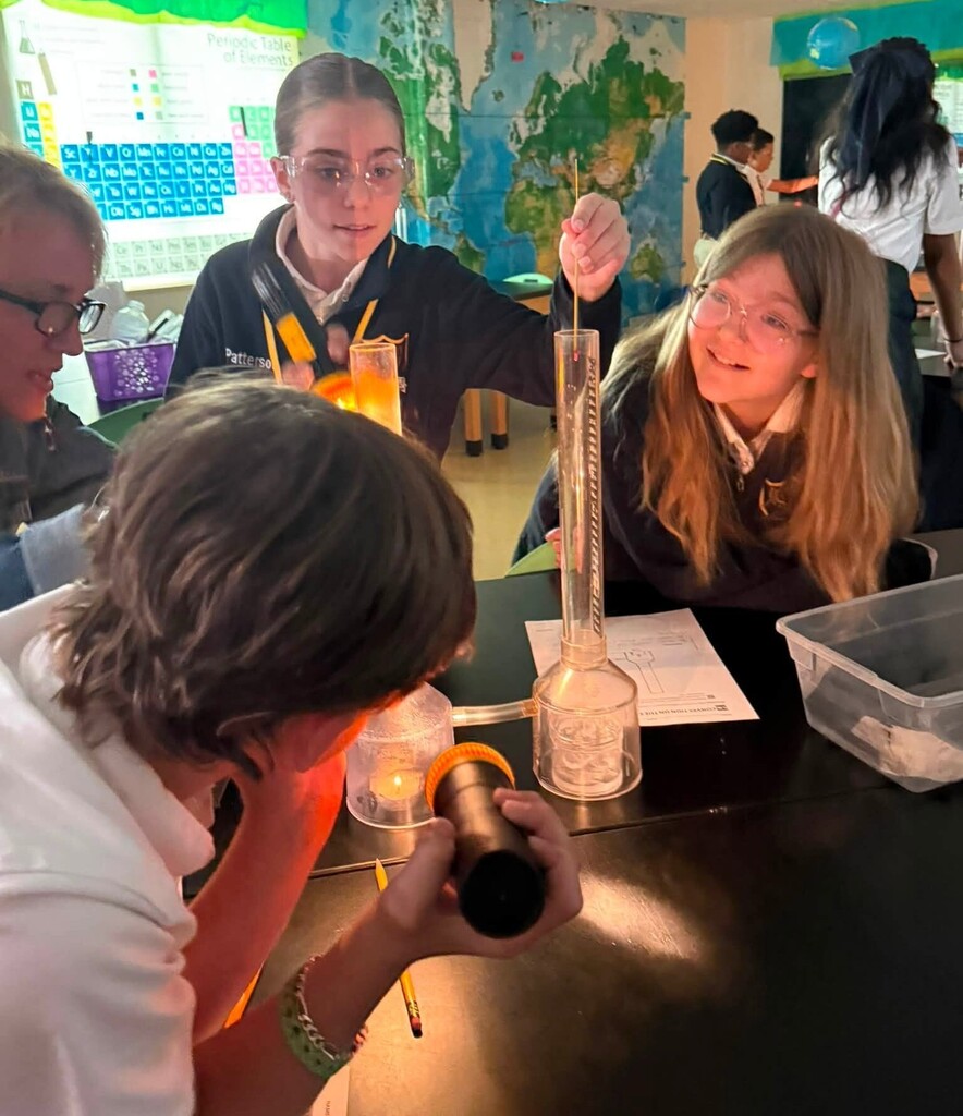 A student drops something into a beaker as others watch