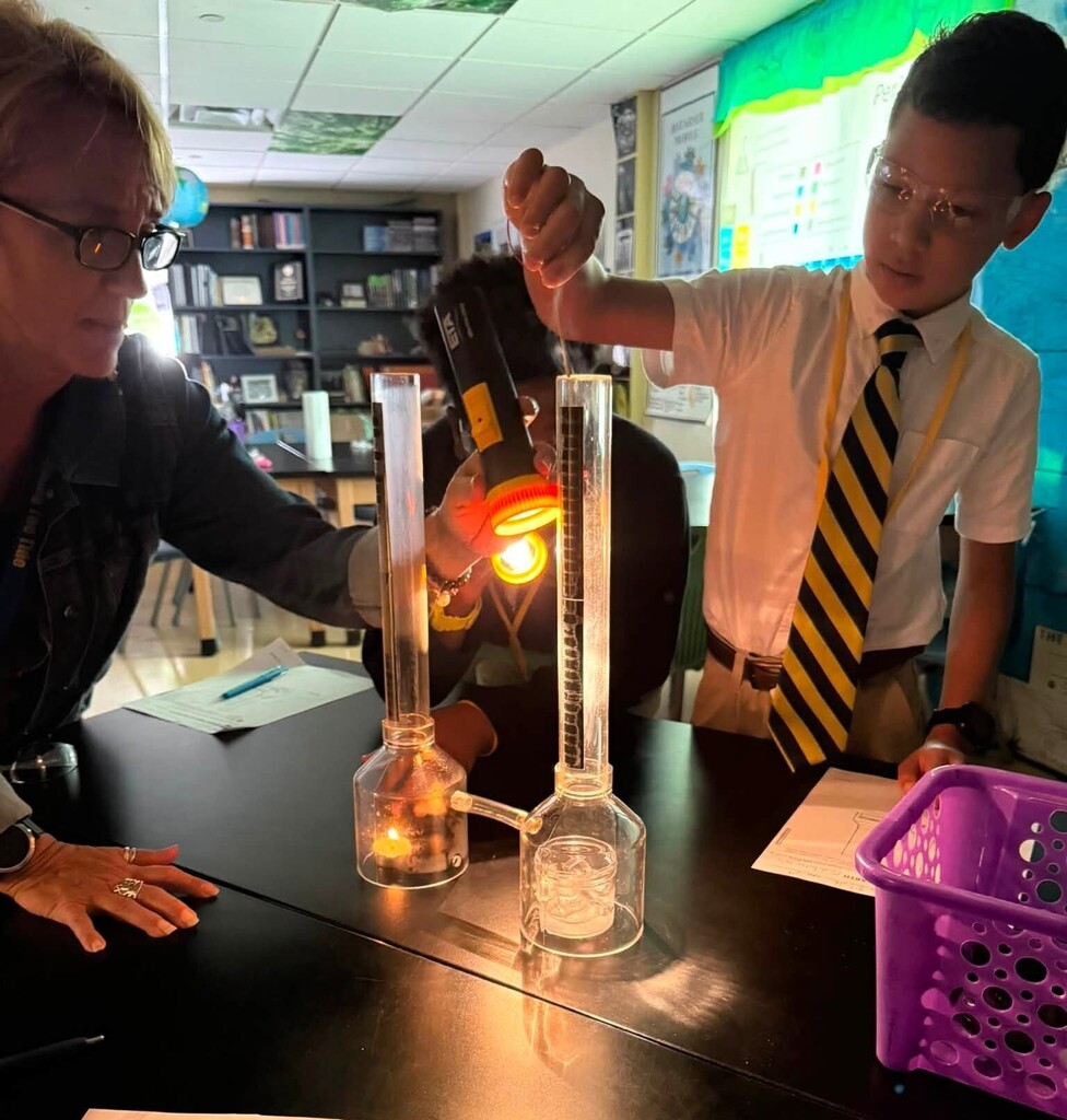 A student drops something into a beaker as his teacher shines a flashlight on it