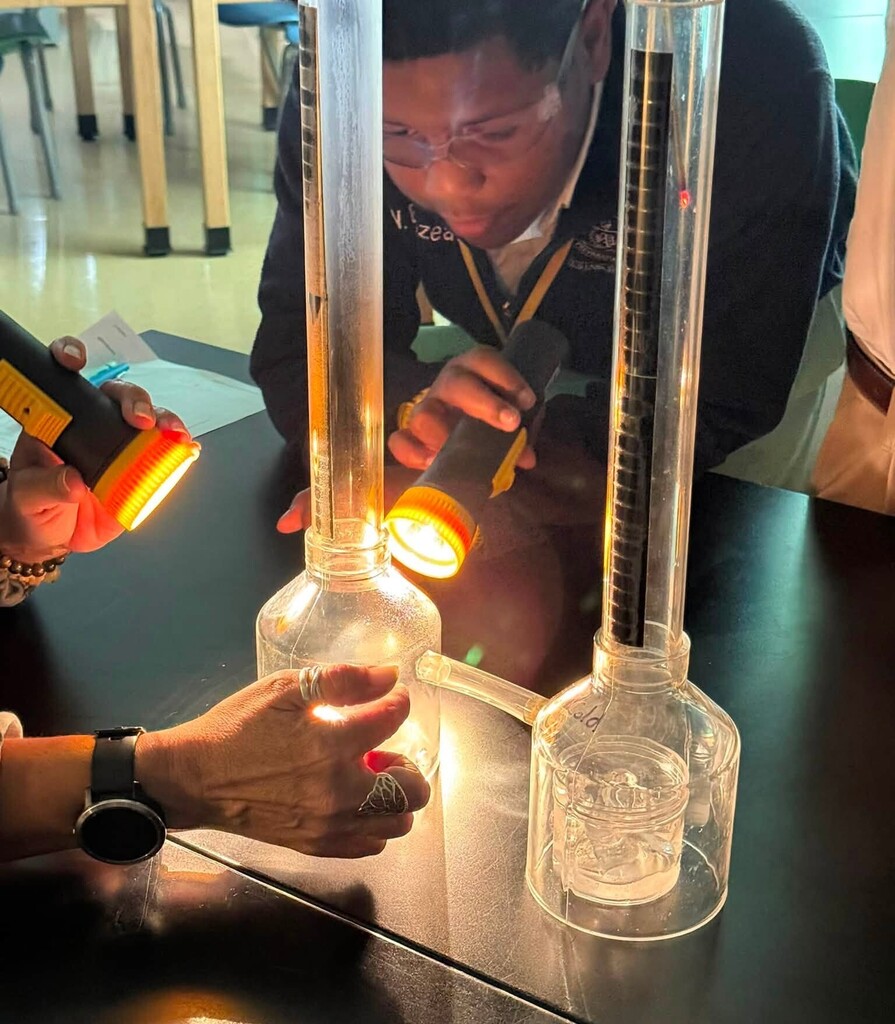 A student shines a flashlight on a beaker as his teacher touches it