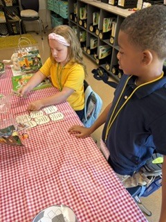Two children seated at a table with a red-and-white tablecloth. They are engaged in an activity involving small objects.