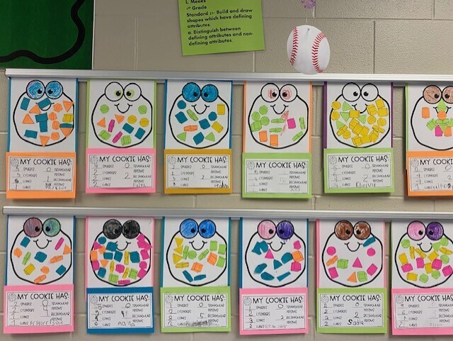 Display of colorful art pieces depicting frog faces. Each piece has mosaic eyes and faces with different colors and shapes. A baseball is on a shelf above.