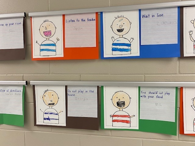 Display of several colorful student art projects. Each project features a simple cartoon character on a piece of paper.