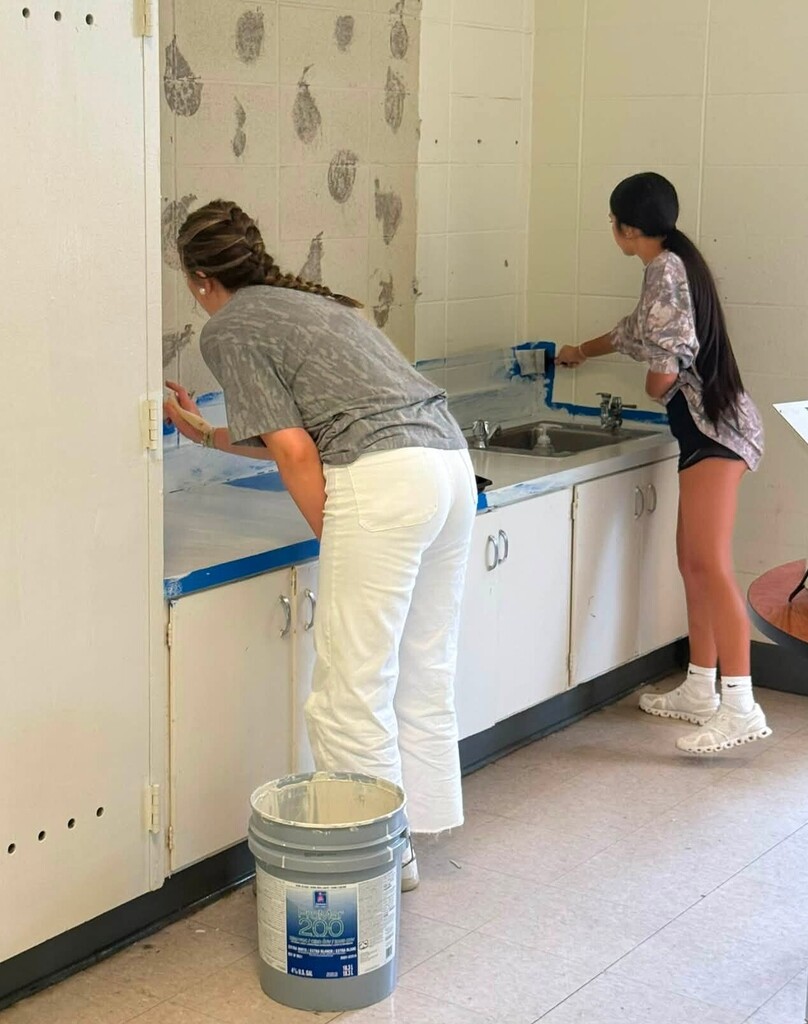 Two girls painting a wall in a school classroom
