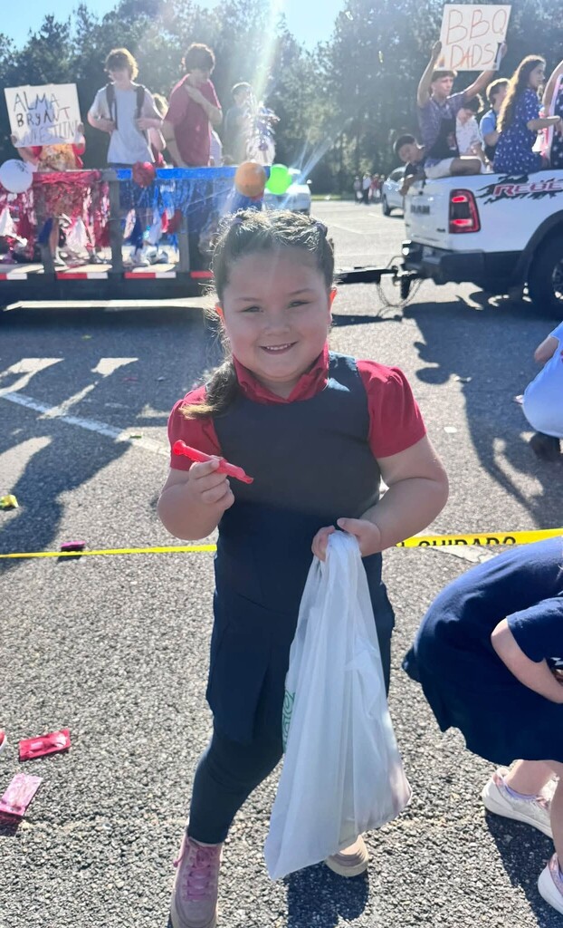 A girl holds a bag and a whistle, as a parade float passes behind her