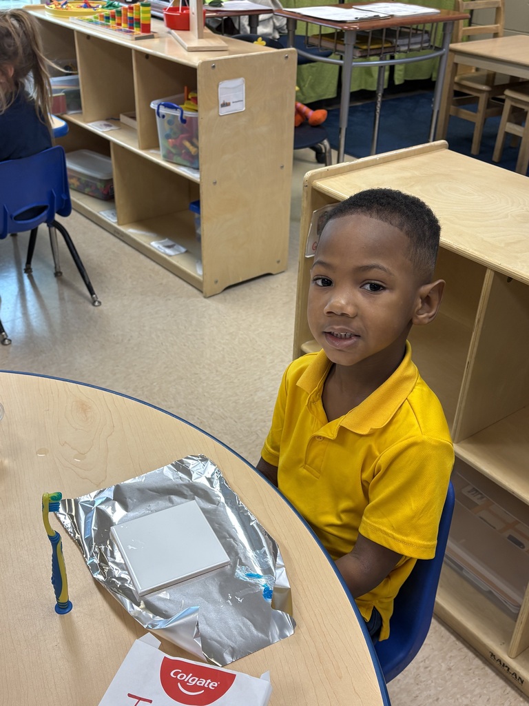 A young child in a yellow polo shirt sits at a table with a foil package and toothbrush.