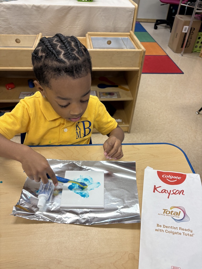 A young boy with braided hair paints on paper atop a foil sheet at a table.
