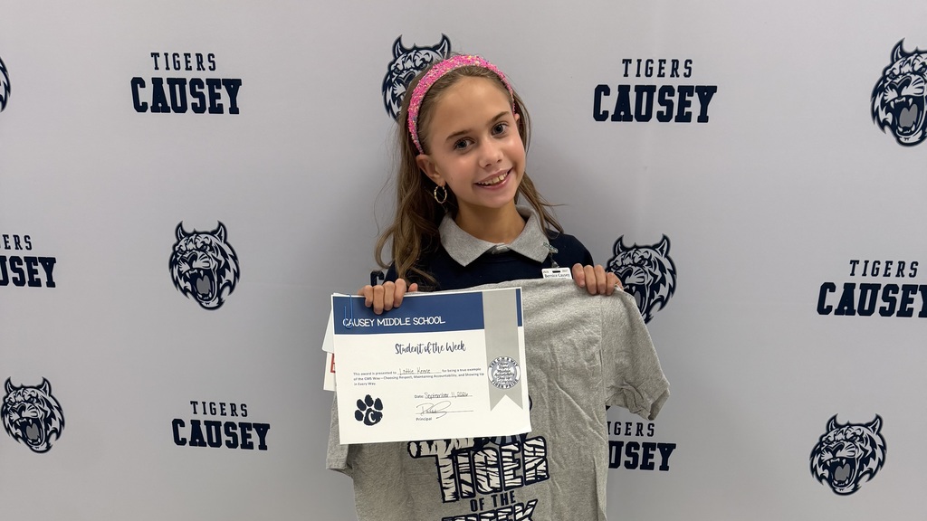 Young girl wearing a headband holds a certificate and a t-shirt against a wall with tiger graphics.