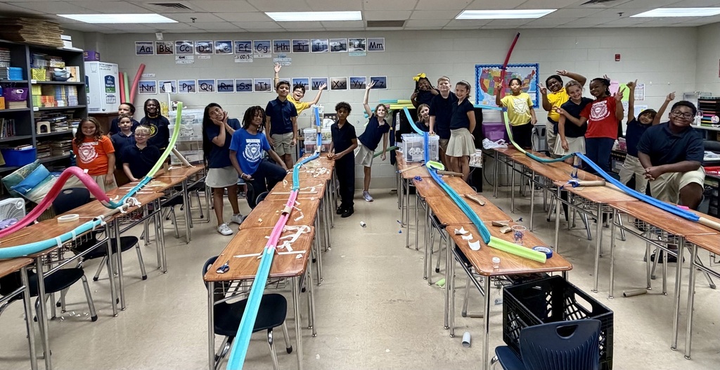 A classroom with desks in rows, students wearing casual attire, and colorful plastic tubes on the tables.