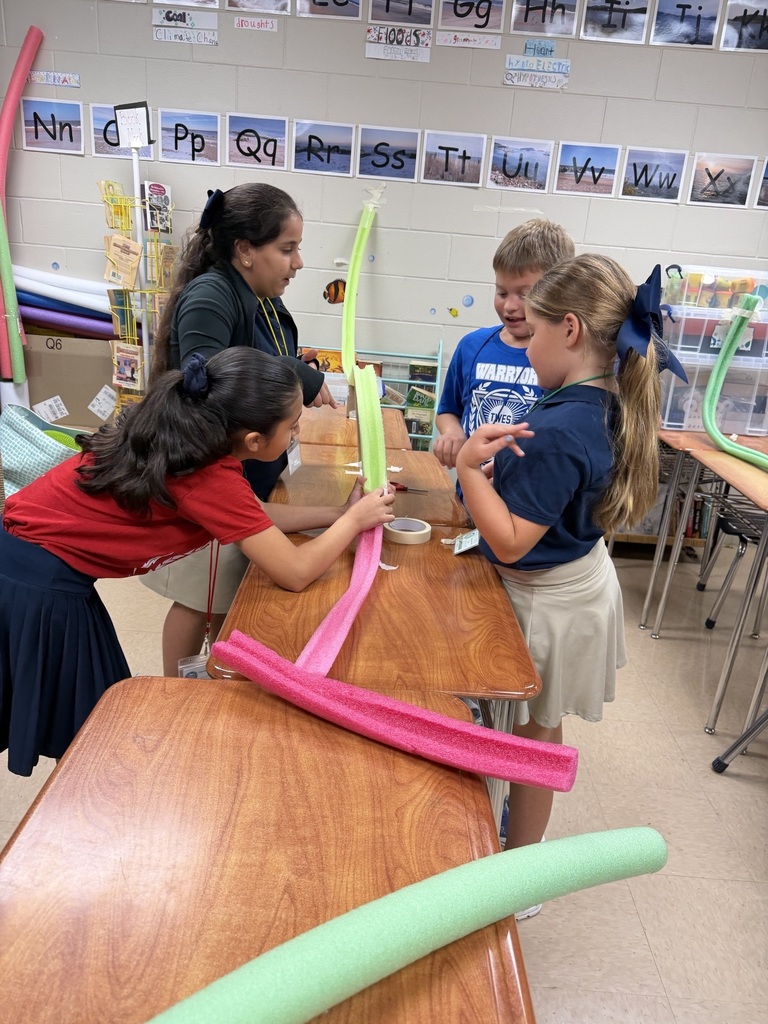Four children in a classroom are standing around a desk, using colorful plastic tubing for a project.