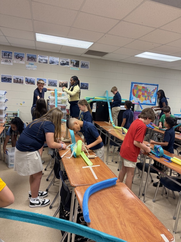 Classroom with students working on a project with blue tubing. Some students are standing and others are seated.