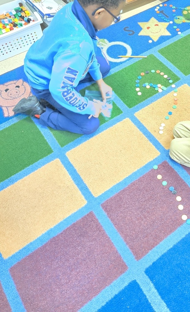 A child arranges colorful beads on a patterned rug. A white storage bin is nearby.