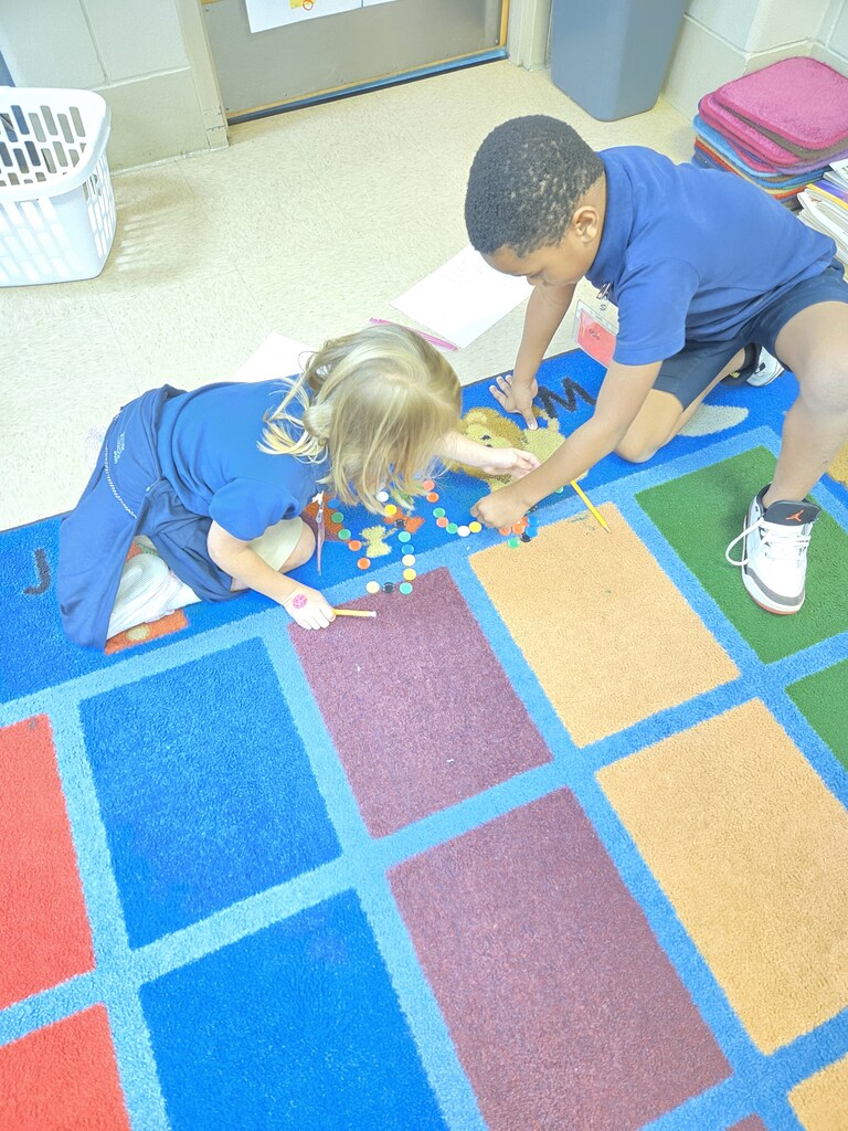 Two children, one in blue, another in white shoes, are playing with colorful building blocks on a multicolored carpet.
