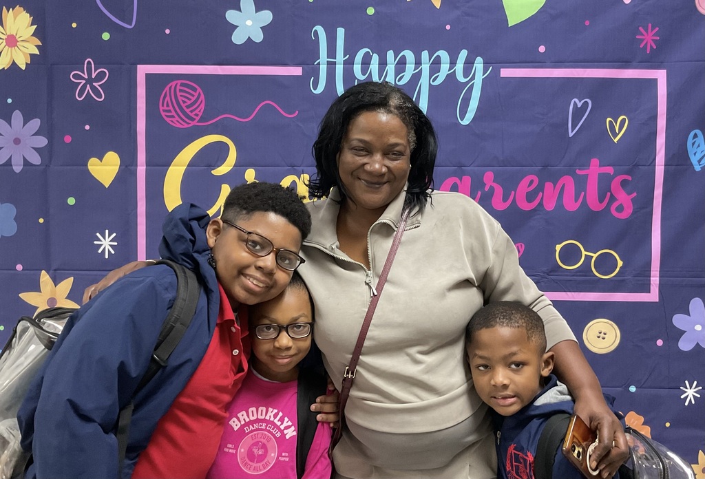 Three children with a woman in front of a colorful backdrop with hearts and flowers.