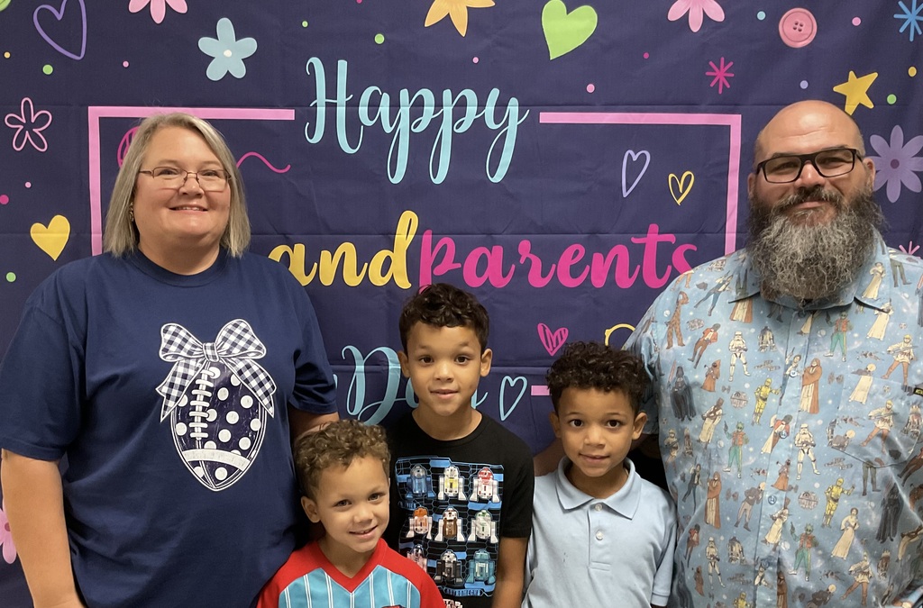 A family of four adults and two children poses for a photo in front of a colorful backdrop with decorative elements.