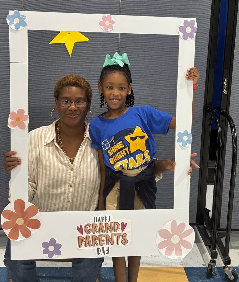 A woman with a girl posing with a frame that reads "Happy Grandparents Day"