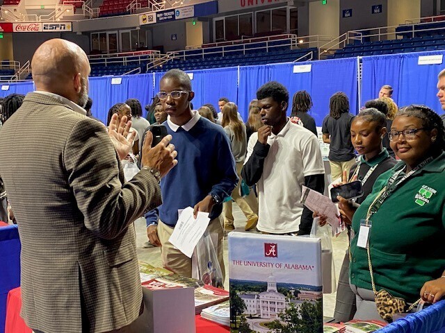 A man at a University of Alabama table talking with students