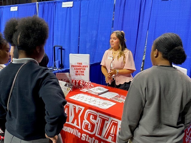 A woman at a Jacksonville State booth talking with students