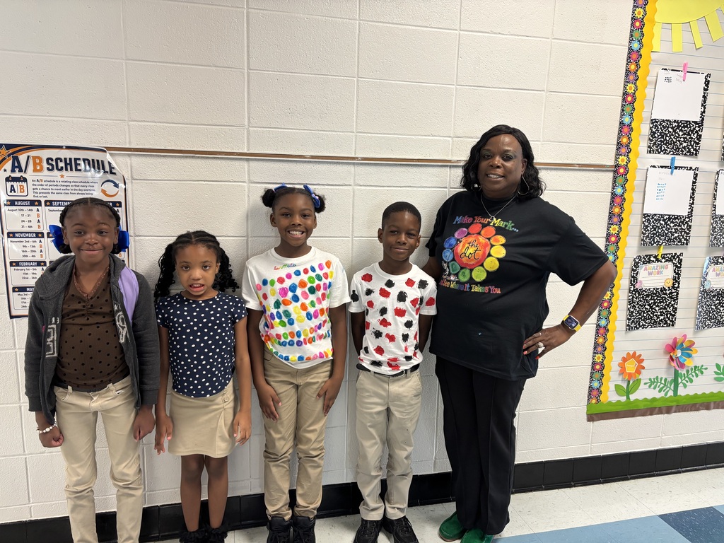 Five children in a classroom. A teacher with them. A calendar and a bulletin board on the wall.