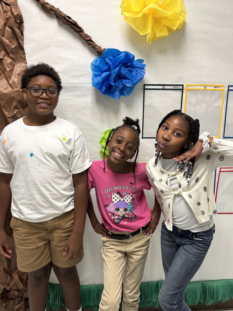 Three kids pose for a picture in front of a wall with blue and yellow paper decorations.