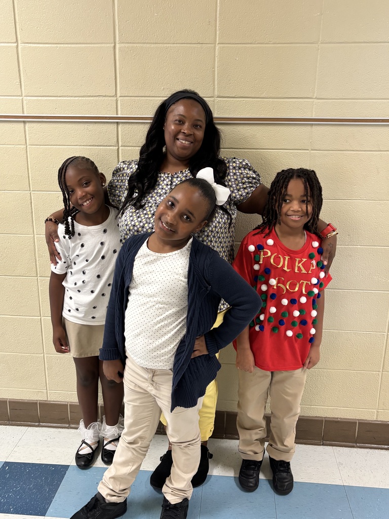 A woman and three children standing together in front of a tiled wall and blue floor.
