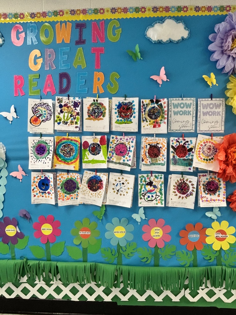 A bulletin board with "Growing Great Readers" text. Displays colorful flowers, butterflies, and student artwork on a blue background.