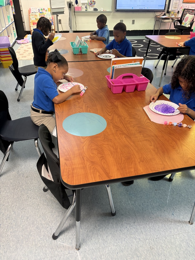 Children seated at a table, engaged in an art activity, with tables and chairs around them.