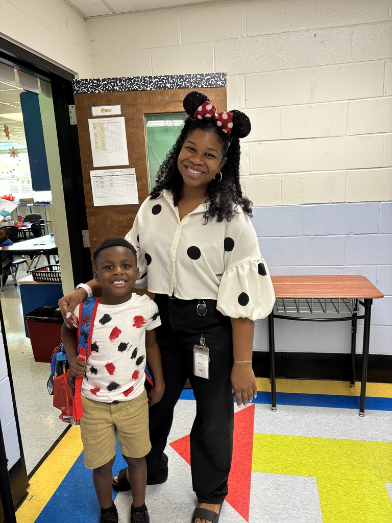 Woman in polka dot shirt with Minnie Mouse ears standing next to a child in a red and white shirt.