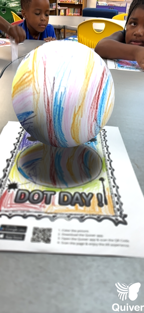 Two children sit at a table with a colorful, drawn ball on top of a Dot Day paper.