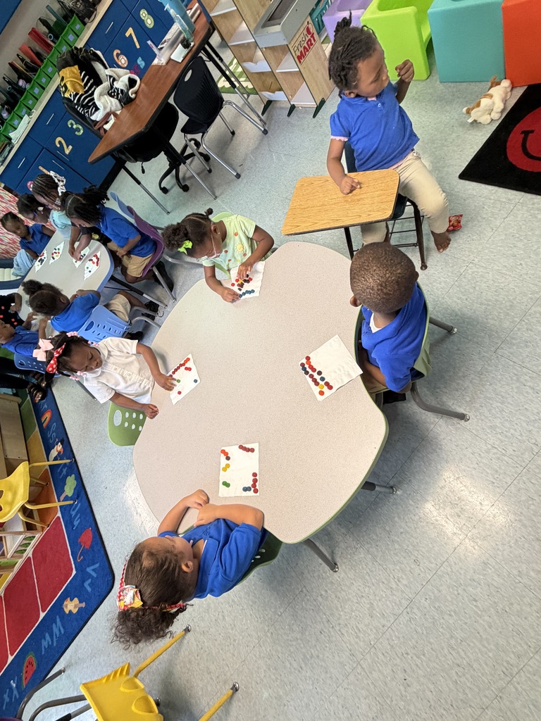 A classroom with several young children seated at a round table, engaged in activities with papers.