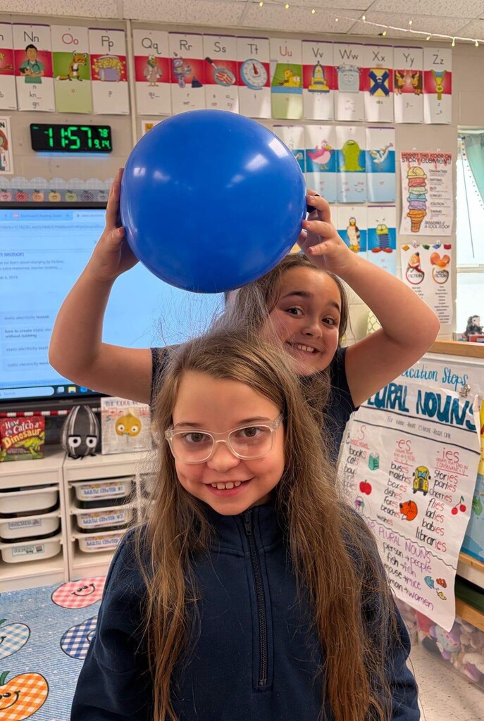 A girl holding a balloon over another girl's hair to show static electricity