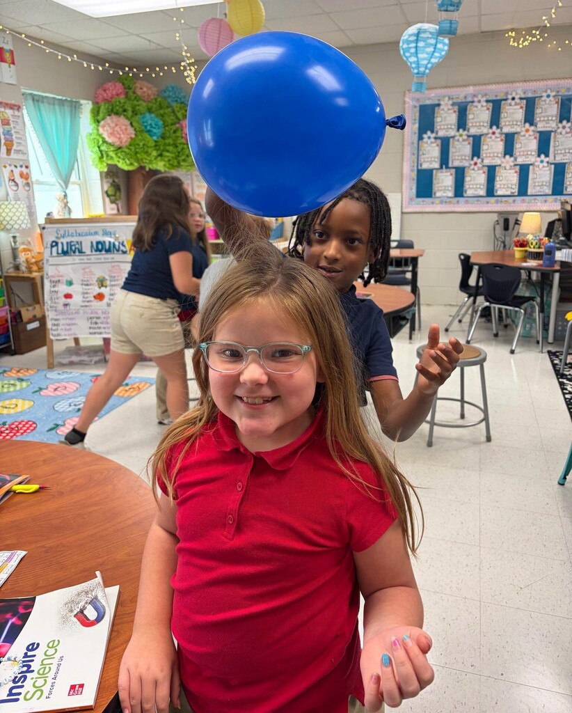 A boy holding a balloon over a girl's hair to display static electricity