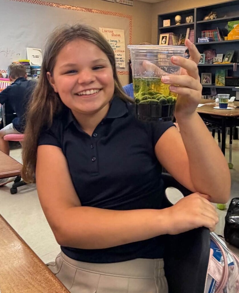 A smiling girl holds a lava lamp in a plastic cup