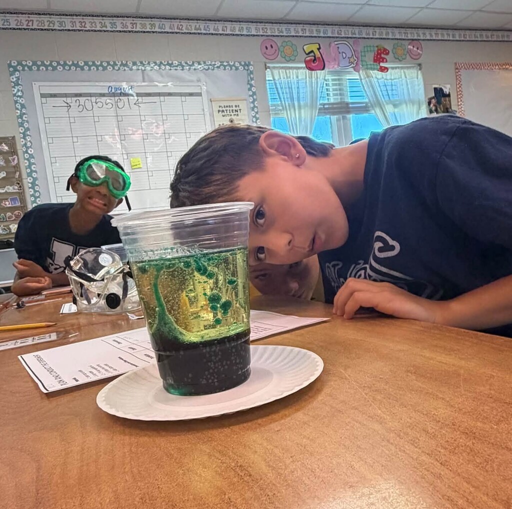 A boy leans down to watch a lava lamp in a plastic cup