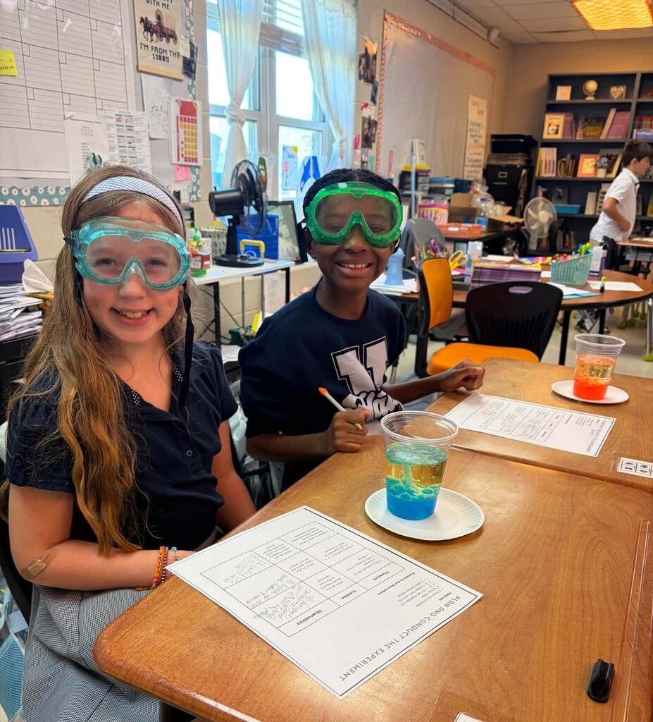 Two smiling students at a desk with lava lamps in plastic cups