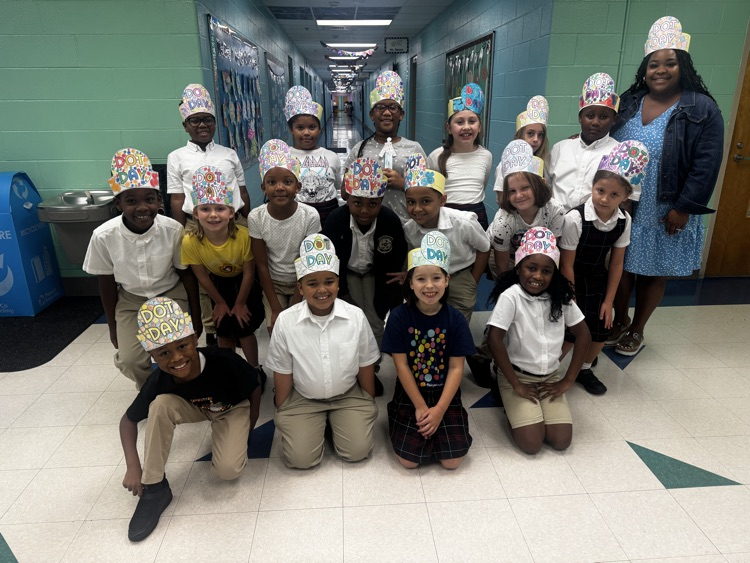 Mrs. Jones stands with her smiling third-grade students in the school hallway as they wear their colorful, handmade Dot Day hats.