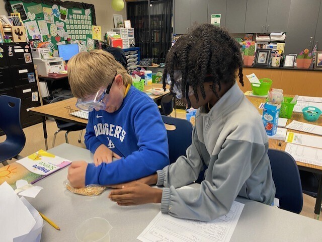 Two children, one wearing a blue sweatshirt and the other a gray one, work together at a table.