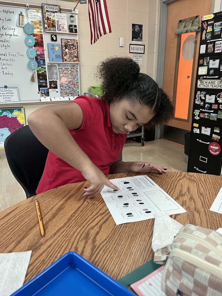 A person sits at a desk, pointing at a piece of paper with various dots and numbers.