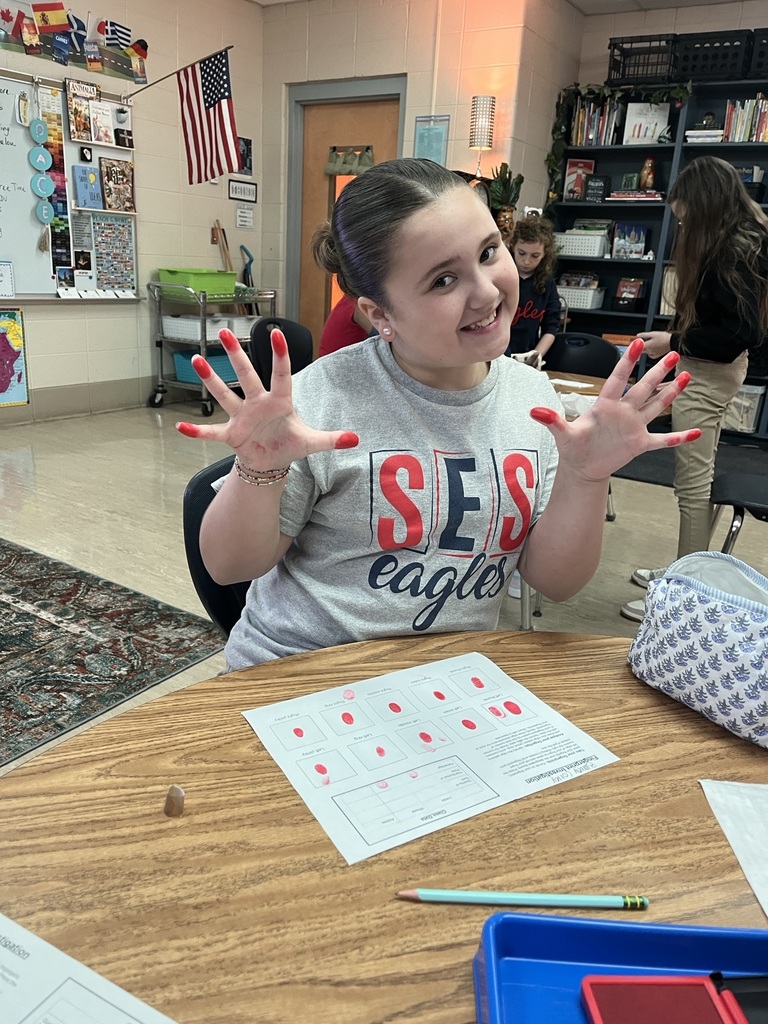 Girl seated at a table with hands painted red, wearing a shirt that reads "SES eagles".