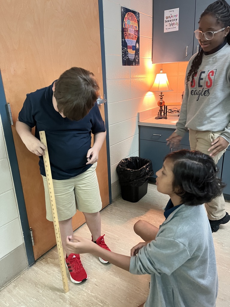 Three students using a tape measure to measure a door. One is standing and the others are sitting.