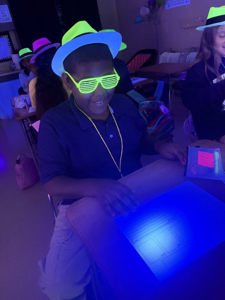 A boy wearing a neon green hat and sunglasses smiles at a table with a blue light.