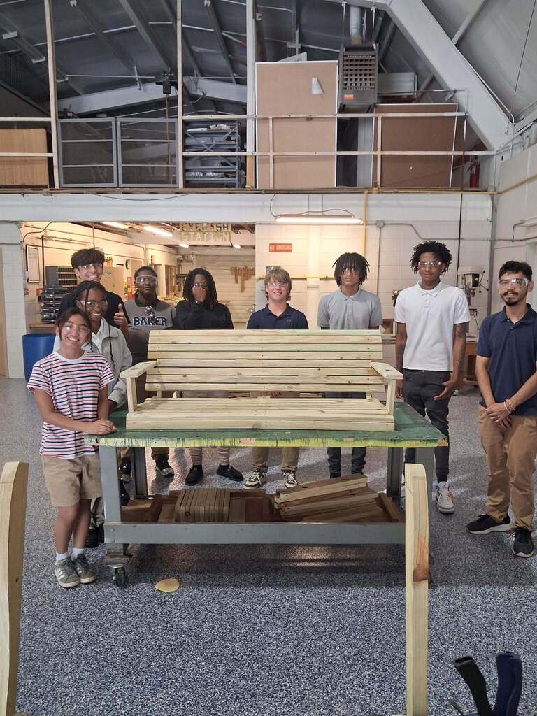 Bryant Career Teach students standing in a workshop beside a wooden swing they constructed.