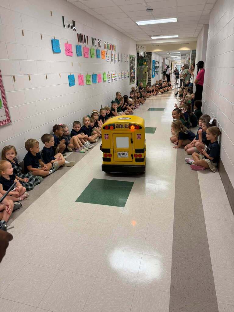 "Buster" the miniature school bus driving down the hall of Tanner Williams Elementary and students watch. 