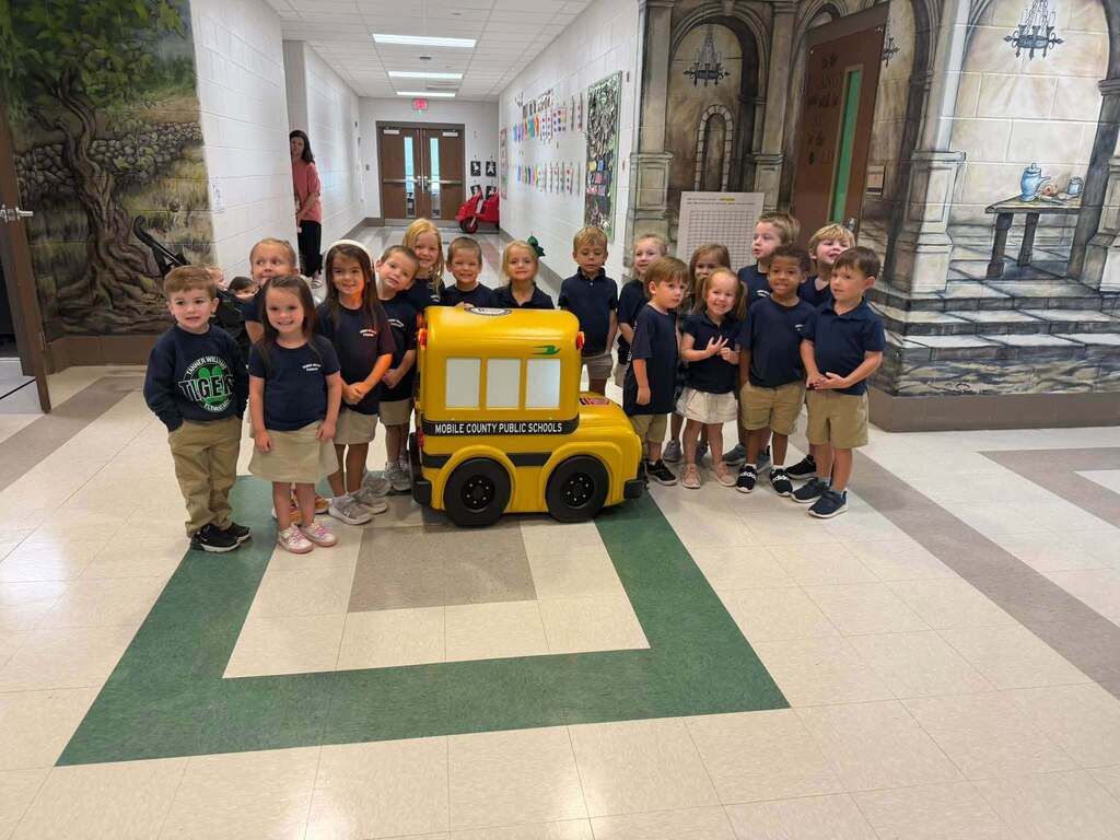 Students at Tanner Williams Elementary smiling beside "Buster" the minature school bus. 