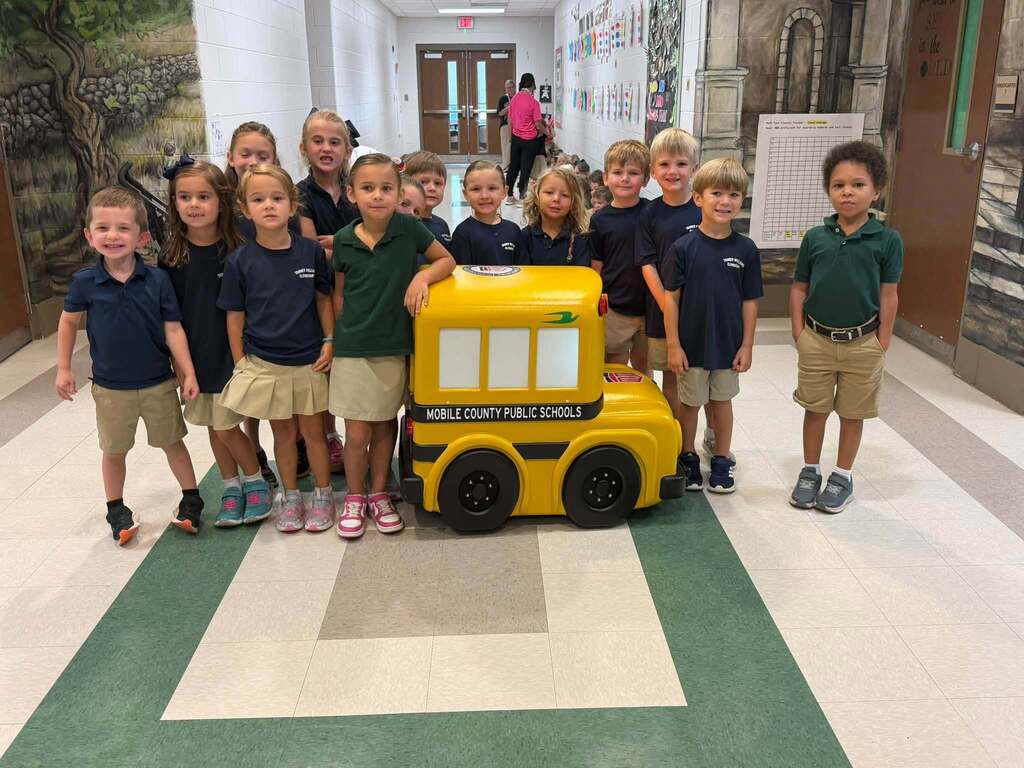 Students at Tanner Williams Elementary smiling beside "Buster" the minature school bus. 