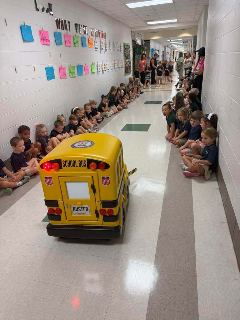 "Buster" the miniature school bus driving down the hall of Tanner Williams Elementary as students watch and smile. 